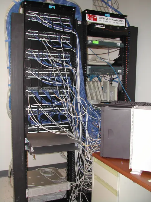 Two computer racks full of cables connected to a couple computers on a nearby table.