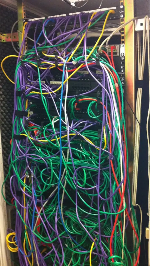Computer rack with a huge mess of crisscrossing network cables of various colours.